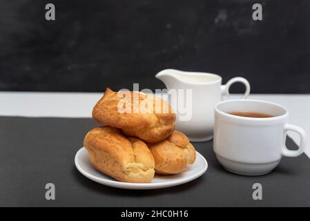 Homemade delicate profiteroles and cup of coffee. Traditional French eclairs. Side view. Stock Photo