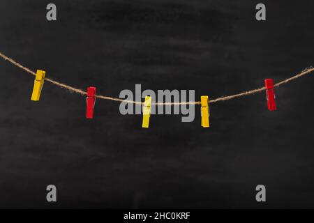Red and yellow clothespins on rope on black background. Space for text, mock up. Stock Photo