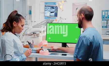 Dentist and nurse looking at green screen on monitor and analyzing teeth layout for stomatological care. Man and woman working with dental equipment for dentistry and teethcare. Stock Photo