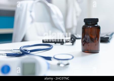 Selective focus on pills bottle standing on table ready for disease consultation. Empty doctor office with nobody in it equipped with professional examination tools. Medicine concept Stock Photo