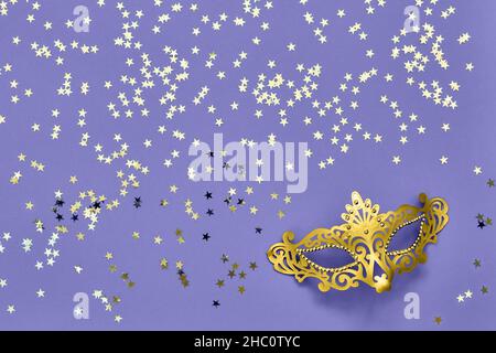 Golden carnival mask and golden stars on lilac very peri background. Top view, copy space. Carnival party celebration concept. Stock Photo