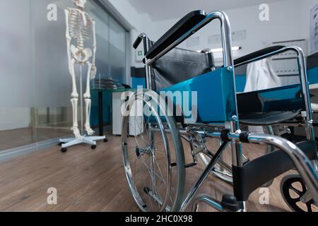 Medical wheelchair standing in empty doctor office with nobody in it used for invalid patient during illness examination. Hospital room equipped with professional instruments. Health care services Stock Photo