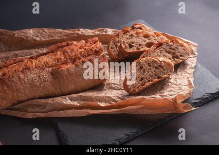 baguette of buckwheat flour without yeast on a black background, slices of sliced bread on parchment paper. Stock Photo