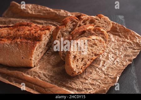 baguette of buckwheat flour without yeast on a black background, slices of sliced bread on parchment paper. Stock Photo