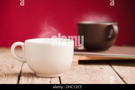 brown cup and off white cup with chocolate, tea or coffee, hot steam,  on rustic wooden table with red background Stock Photo