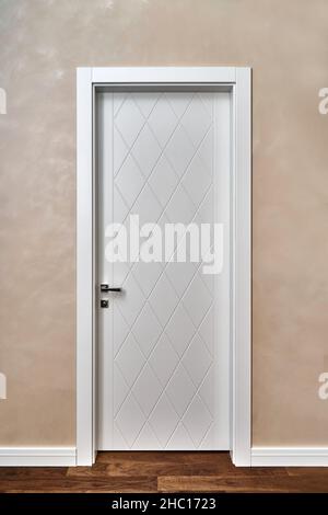 Stylish contemporary white door decorated with rhombus pattern in light room with painted beige wall and wooden parquet floor Stock Photo