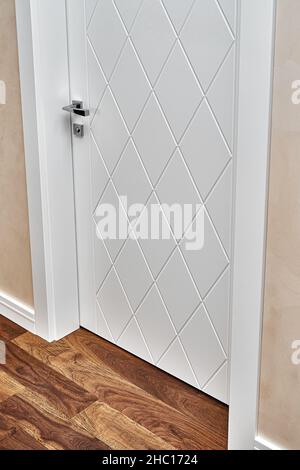 Stylish contemporary white door decorated with rhombus pattern in light room with painted beige wall and wooden parquet floor closeup Stock Photo
