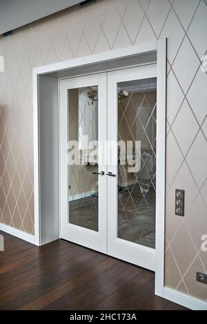 Elegant trendy inner doors with rhombus pattern on glass surface and silver handles in light spacious room of renovated apartment Stock Photo