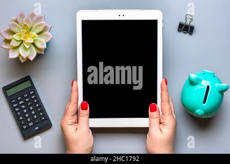 female hands holds digital tablet with black screen, piggy bank, calculator, succulent, notebook on gray background Business, insurance, technology co Stock Photo