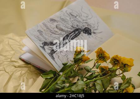 A drawing in a notebook and a fading bouquet of yellow roses. Sketch of a depressed teenager walking with his head down. Pessimistic thoughts fly arou Stock Photo