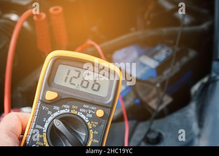 Mechanic hand use multimeter voltmeter to check the voltage level in a car battery. Stock Photo