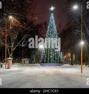 Artificial Christmas or New Year tree decorated with garlands in a winter night park with glowing lanterns. Stock Photo