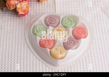 Flower shape colourful cookies in heart shape gift box on white cloth.  A gift box for New Year, Christmas or Valentine’s Day. Stock Photo