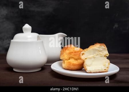 Sweet eclair cake with cream filling on white plate and tea set. Pastry sweets. Baking for tea. Stock Photo