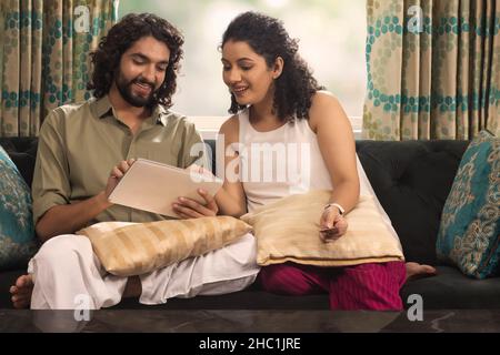Young couple selecting items during  online shopping while sitting on sofa at home Stock Photo