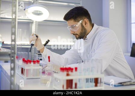 Serious young male scientist using a pipette while working in the pharma laboratory Stock Photo