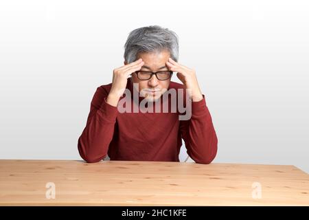 The Senior Asian man sitting at the desk on the white background. Stock Photo
