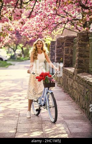 Spring style travel. retro woman sell tulip flower bouquet. girl under sakura with vintage bicycle. spring beauty and fashion. cherry tree pink Stock Photo