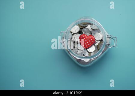 Red heart and coins in a jar on light green background  Stock Photo