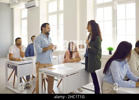 Business coach training group of adult people who are sitting at desks in classroom Stock Photo