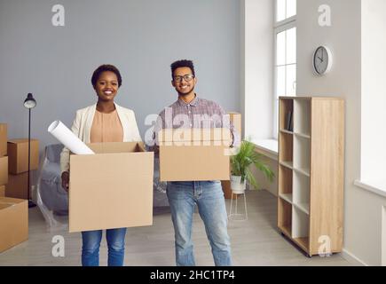 Happy, smiling young couple moving into a new house and carrying cardboard boxes together Stock Photo