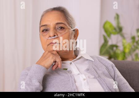 Old woman sitting on sofa with nasal cannula at home Stock Photo