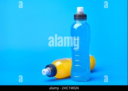 Standing and lying isotonic energy orange yellow and blue sport drink in plastic bottles on blue background. Allows to maintain the most optimal balance of water Stock Photo