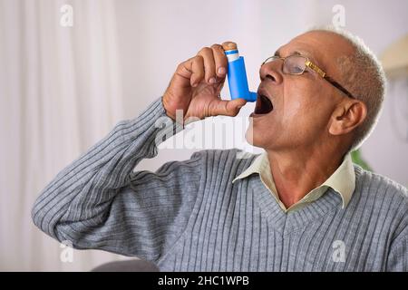 Old age man using her Asthma Inhaler at home Stock Photo