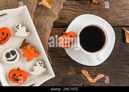Autumn composition of orange and white biscuits for Halloween, a cup of coffee, autumn leaves on a brown wooden table. Stock Photo