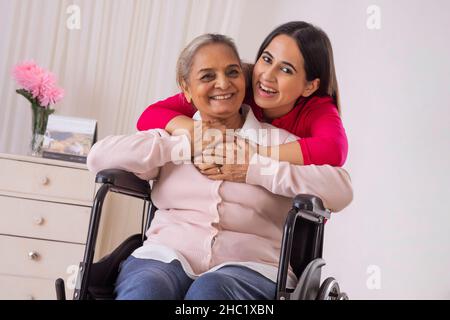 Granddaughter hugging her grandmother from backside while sitting on wheel chair Stock Photo