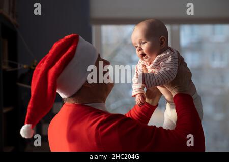 Caucasian grandfather in red hat playing with granddaughter at home selebrating Christmas Stock Photo