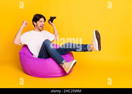 Portrait of attractive lucky cheerful guy playing game having fun rejoicing triumph isolated over bright yellow color background Stock Photo
