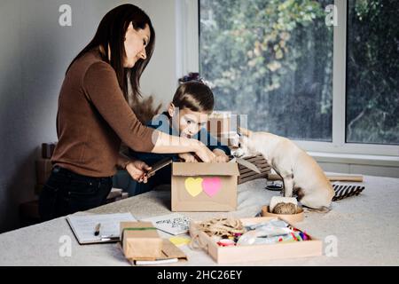 Charity Care box, donation box, gift package ideas. Happy family, mother, kid and dog putting staff into donation box. Care Package Delivery, Winter Stock Photo