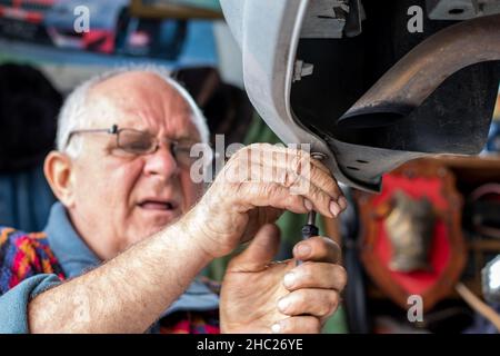 Portrait of an old car mechanic checking and repairing a lifted automobile in his garage. Tinsmith working on a car. Old car mechanics and repair. Stock Photo