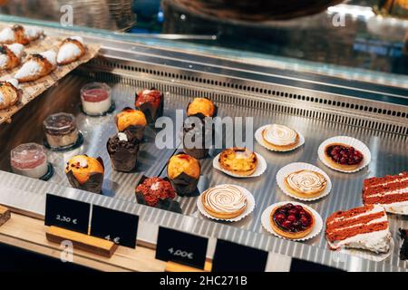 Various cakes are on plates in a display case with price tags Stock Photo