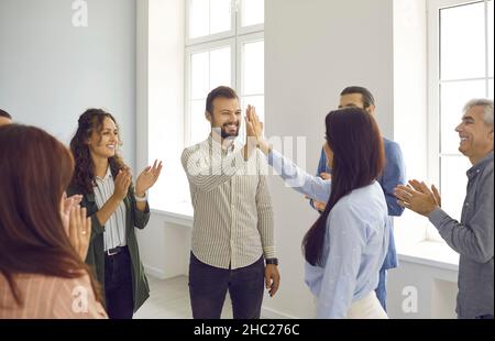 Happy man and woman giving each other five to applause of colleagues after seminar training. Stock Photo