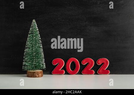 Artificial Christmas tree and red numbers 2022 on black background. New year concept. Copy space. Stock Photo