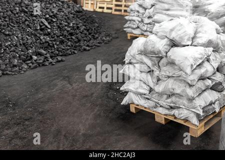 Big heap of dark black lump coal on floor bulk. Charcoal sorage at warehouse stock reserve. activated anthracite packed in plastic bag sack on wooden Stock Photo