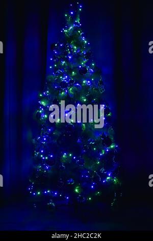 Decorated Christmas tree in the dark, glowing green and blue lights Stock Photo