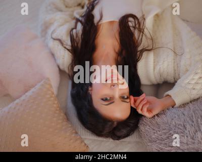 Lovely brunette woman posing in a bedroom. Good morning. Playful charming young woman lying in bed, stretching, having great plans for day. Cute lady lazing in her bedroom, smiling happily Stock Photo