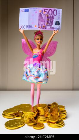 Barbie doll holding a 500 Euro banknote, stack of Euro coins chocolates, wrapped with embossed 1 Euro coin golden foil, Stock Photo