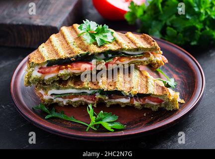 Vegetarian sandwich panini with spinach leaves, tomatoes and cheese on a dark table. Toast with cheese. Stock Photo