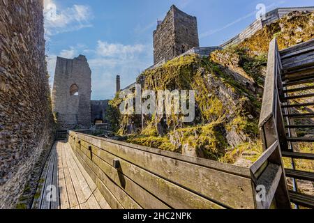 Wooden walkway with a tower in the background, staircase going up a rocky hill covered with green moss, stone tower at Brandenbourg castle on top, sun Stock Photo