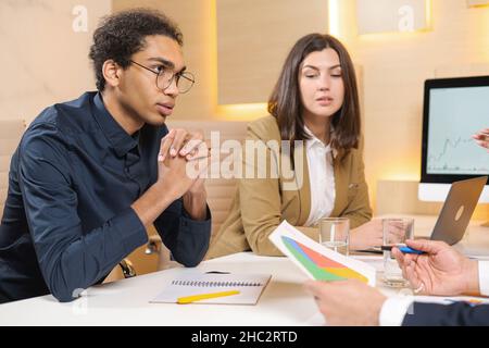 Going over details. Group of young confident business people discussing something while spending time in the office. Male office worker looking at colleagues while discussing something Stock Photo