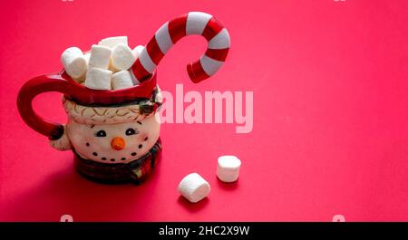 Christmas hot beverage, chocolate mug with marshmallows and candy cane on red color background, space. Winter holiday sweet drink Stock Photo