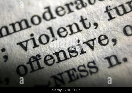 Word "offensive" and "violent" printed on dictionary page, macro close-up Stock Photo