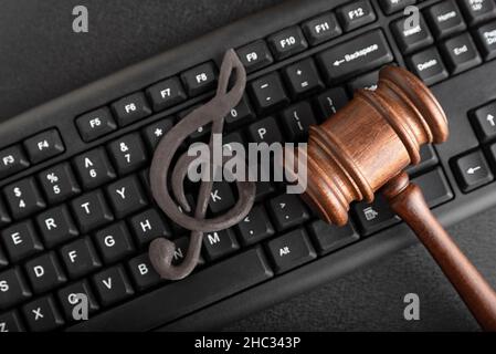 Protection of music as intellectual property. Treble clef on the keyboard next to the wooden gavel on black background. Music Licensing Stock Photo