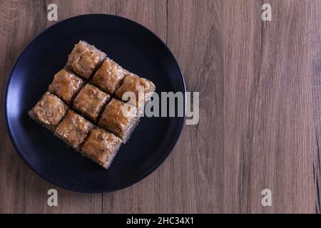 Baklava, traditional Turkish dessert named as Baklava in a black plate on a wooden background. Selective focus on the center baklava. Ramadan concept Stock Photo