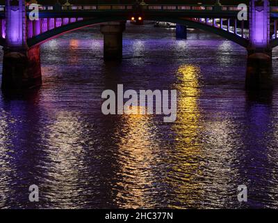 Multi coloured lights reflecting on the River Thames on a winters night with a bridge in the background, London. Stock Photo