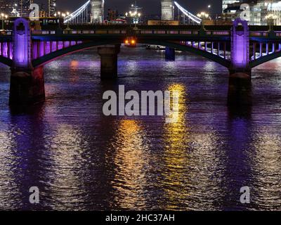 Multi coloured lights reflecting on the River Thames on a winters night with a bridge and Tower Bridge, London. Stock Photo